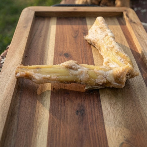 Dog bone treat on a wooden cutting board with a dog in the background