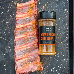 Ribs with a jar of Brown Sugar Chili Rub on a dark surface