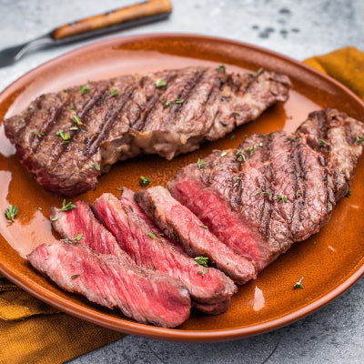 Bison steak on a plate with a close-up of sliced steak, garnished with herbs.
