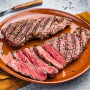 Bison steak on a plate with a close-up of sliced steak, garnished with herbs.